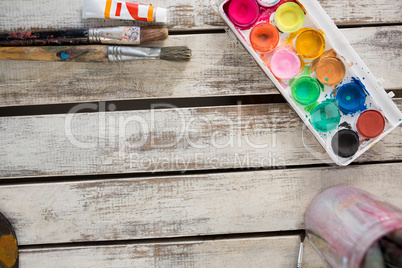 Watercolor paints, palette and paint brushes on wooden surface