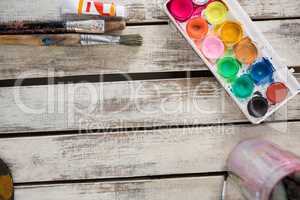 Watercolor paints, palette and paint brushes on wooden surface