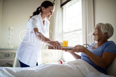 Female doctor serving breakfast to senior woman in the bedroom