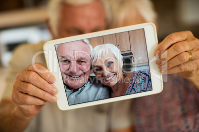 Senior couple taking selfie from digital tablet in kitchen