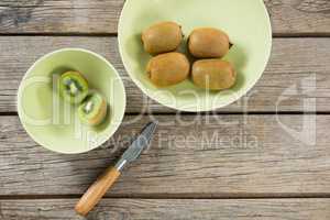 Kiwis in bowl with knife on wooden table