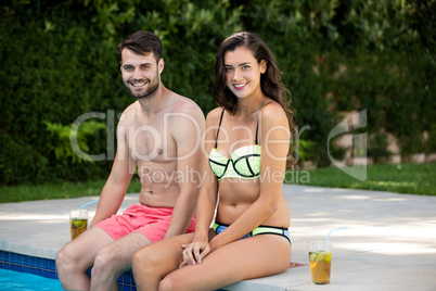 Portrait of young couple sitting at poolside