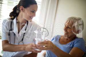 Female doctor serving a water glass to senior woman in the bedroom