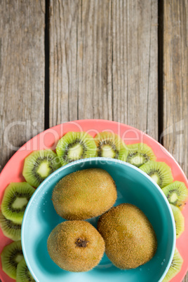 Kiwis arranged in bowl and plate on wooden table