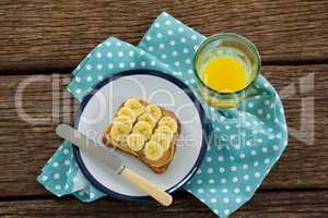 Sliced bananas spred on brown bread in plate with glass of juice