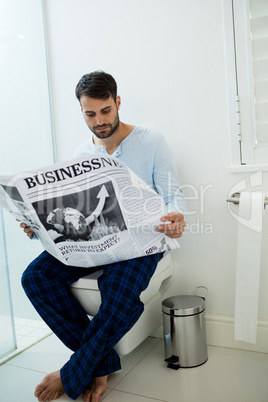 Man sitting on toilet seat reading a newspaper