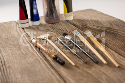 Paintbrushes and watercolor tubes arranged on wooden surface
