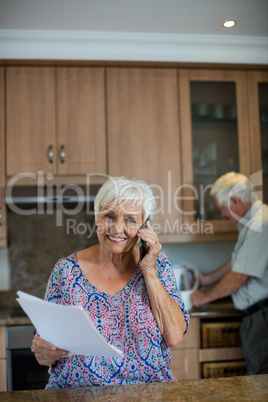 Senior woman talking on mobile phone while man working in kitchen