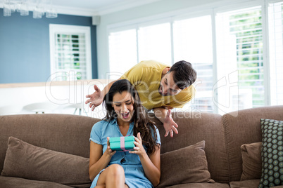 Young man giving a surprise gift to woman in the living room