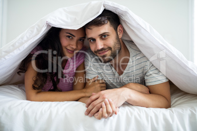 Portrait of happy couple under blanket in the bedroom