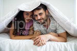 Portrait of happy couple under blanket in the bedroom