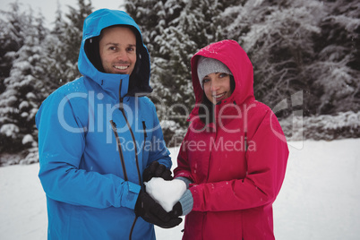 Smiling couple in warm clothing holding snowy heart