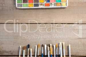 Colorful paintbrush and palette arranged on wooden surface