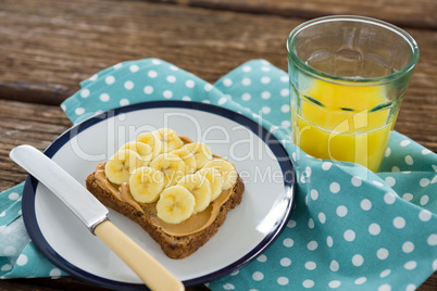 Sliced bananas spred on brown bread in plate with glass of juice