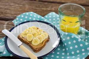 Sliced bananas spred on brown bread in plate with glass of juice