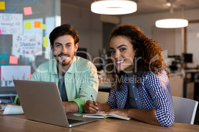 Smiling creative business people with laptop working at desk in office