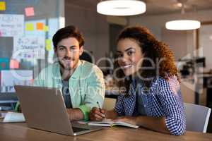 Smiling creative business people with laptop working at desk in office