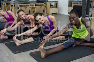 Women performing stretching exercise on exercise mat in gym