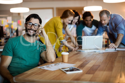 Man leaning on desk while  team working in background