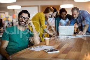 Man leaning on desk while  team working in background