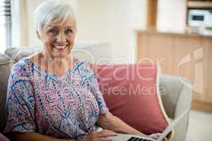 Portrait of happy senior woman using laptop in living room