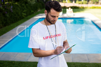 Lifeguard writing on clipboard at poolside