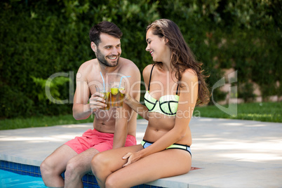 Young couple toasting glasses of iced tea at poolside