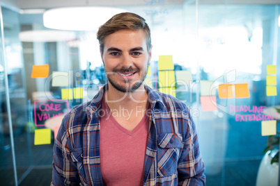 Smiling man standing against sticky notes on the glass wall in office