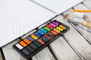 Colorful palette, paintbrushes and book on wooden surface