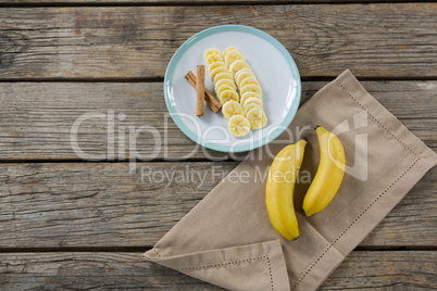 Banana and slices of banana with cinnamon stick in plate on wooden table