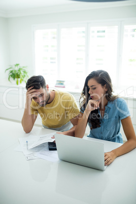 Worried couple calculating their bills with laptop in the kitchen