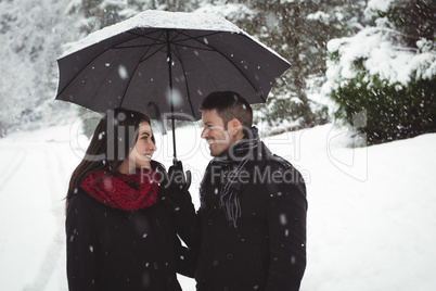 Smiling couple under umbrella standing in forest