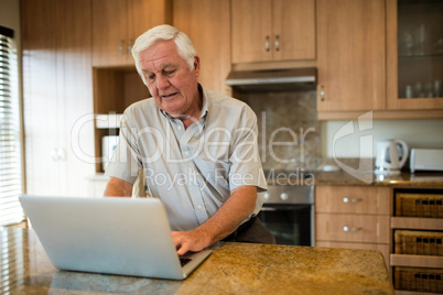 Senior man using laptop in the kitchen