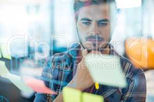 Thoughtful man reading sticky notes on the glass wall