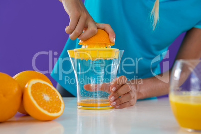 Woman preparing orange juice from juicer against violet background