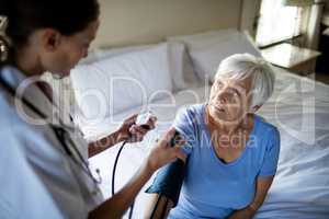 Female doctor checking the blood pressure of senior woman in the bedroom
