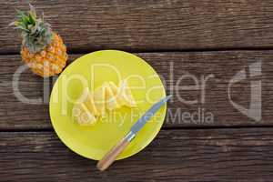 Slices of pineapple in plate on wooden table