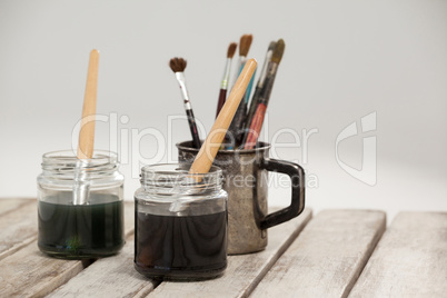 Jars of watercolor and paint brushes on wooden table