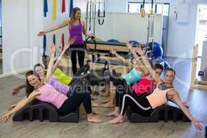 Female trainer assisting group of women with stretching exercise on arc barrel