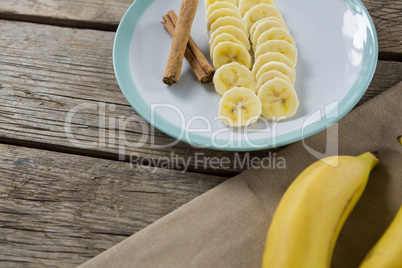 Banana and slices of banana with cinnamon stick in plate on wooden table