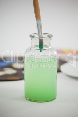 Paintbrush with green paint dipped into a jar filled with water