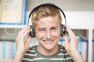 Portrait of happy schoolboy listening music on headphones in library