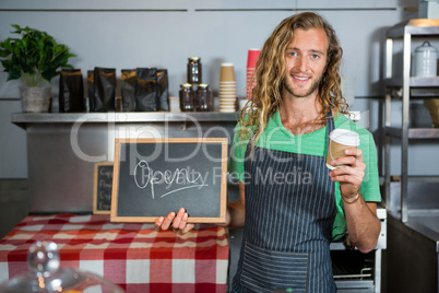 Male staff holding a board with open sign and disposable coffee cup