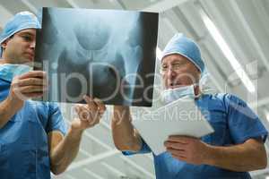 Male surgeons holding digital tablet while discussing x-ray