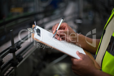 Factory worker writing on notepad in factory