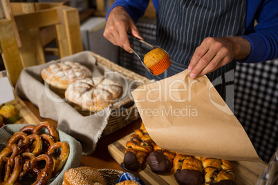 Mid section of staff packing cup cake in paper bag at counter