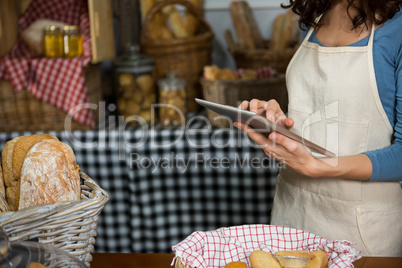 Mid-section of staff using digital tablet at bakery counter