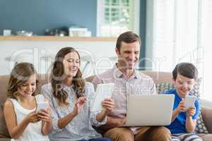 Smiling family using digital tablet, phone and laptop in living room