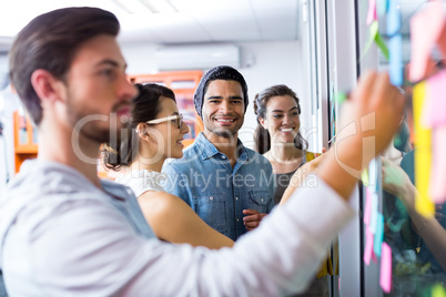 Executives writing on sticky notes on glass wall