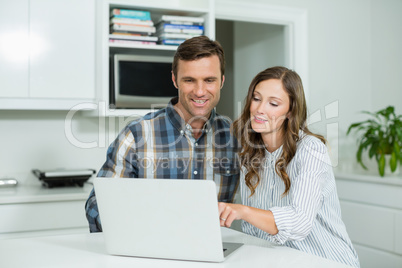 Happy couple interacting with each other while using laptop in living room